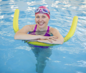 woman in pool with a pool noodle smiling